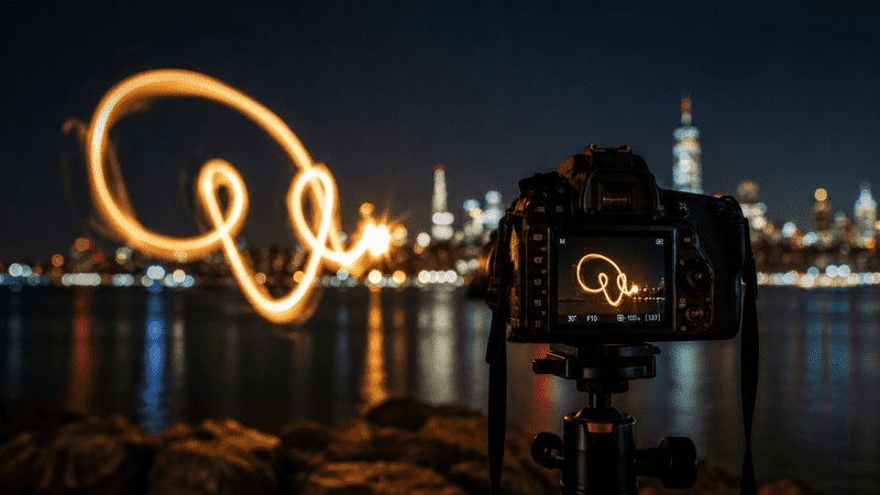 Professional long-exposure light painting with glowing orange trails against a dark background.