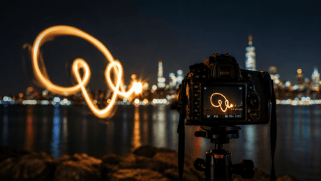 Professional long-exposure light painting with glowing orange trails against a dark background.