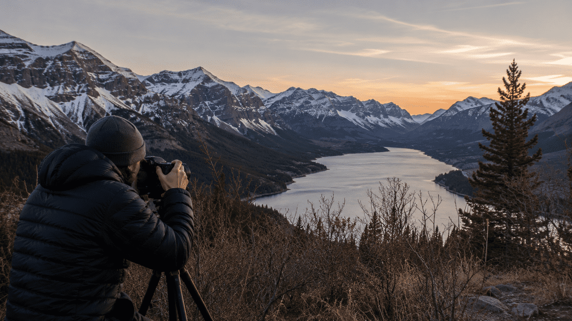 Landscape photographer using a tripod to capture a mountain lake at sunset.