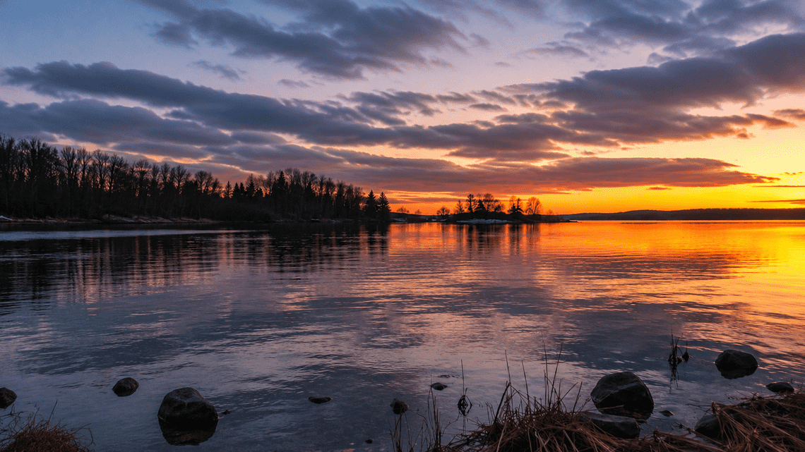Tranquil lake reflecting vibrant orange and purple colors after sunset beneath a dramatic cloudy sky