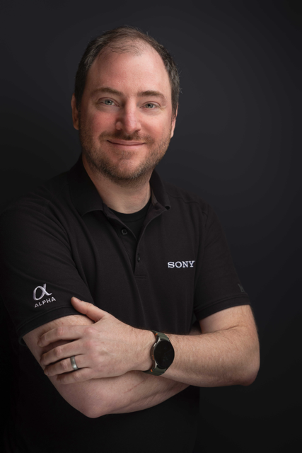 Man wearing a black shirt with Sony logo against a dark background