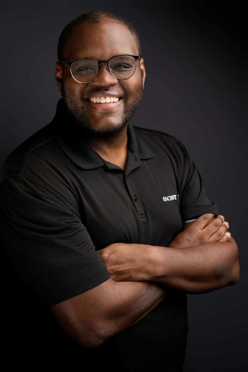 Man wearing a black polo shirt with a logo on a dark background