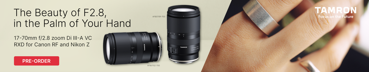 Two camera lenses with a hand wearing a silver ring, featuring Tamron branding.