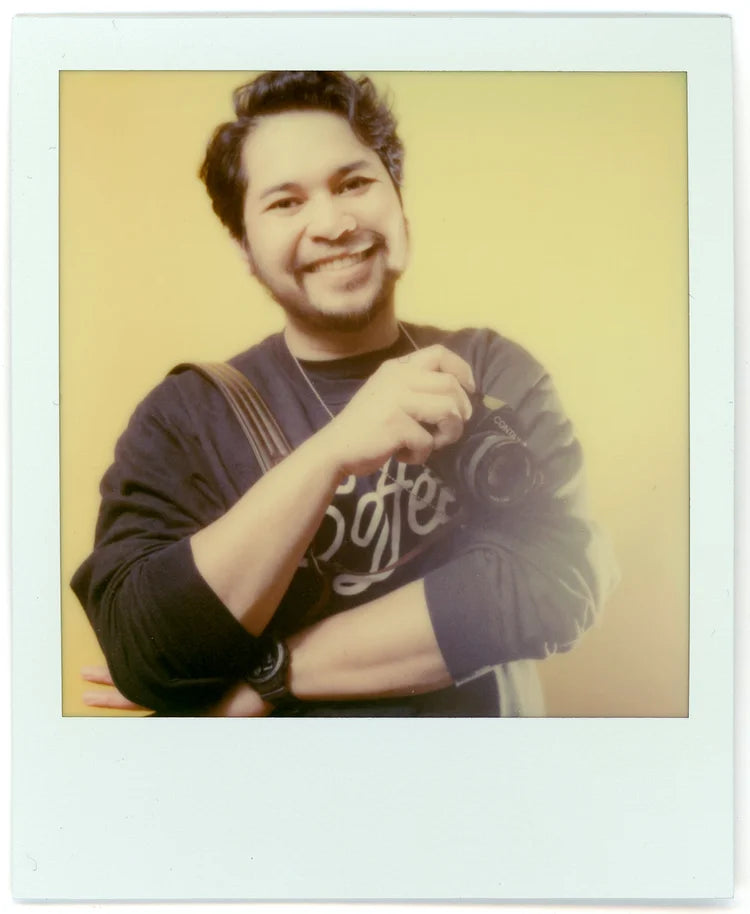 Polaroid-style photo of a person wearing a dark shirt with text, smiling.